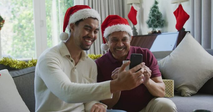 Happy biracial son with father in santa hats doing video call on smartphone in christmas