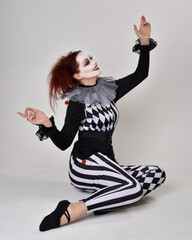 Full length  portrait of red haired  girl wearing a black and white clown jester costume,...