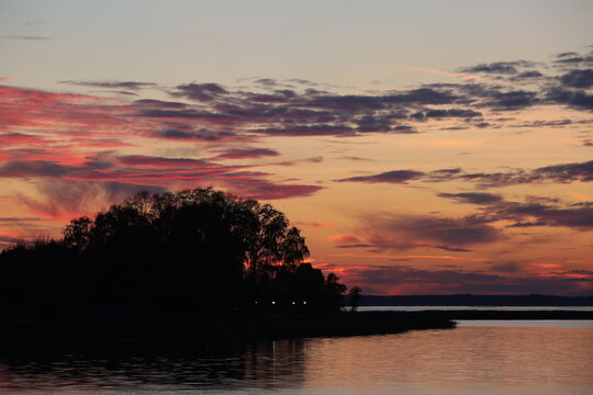 Sunset over a lake with a purple sky and the lights of a human dwelling in the black silhouette of trees on the shore