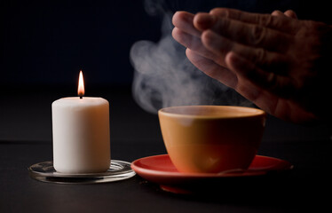 candle with flame, with yellow cup and smoke, hands warming with the heat of the drink, (focus on candle)