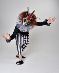 Full length  portrait of red haired  girl wearing a black and white clown jester costume,...