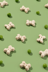 Pattern with dry dog food and peas on green background. Healthy vegan nutrition in bone shape
