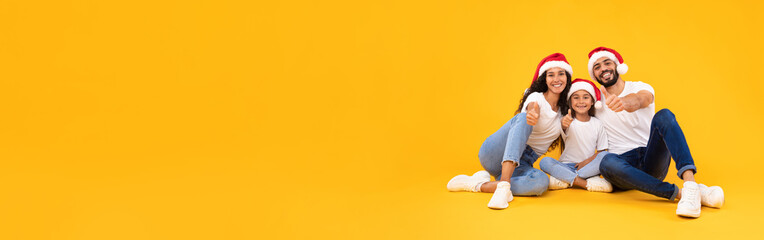 Middle Eastern Family Wearing Santa Hats Gesturing Thumbs Up, Yellow Background