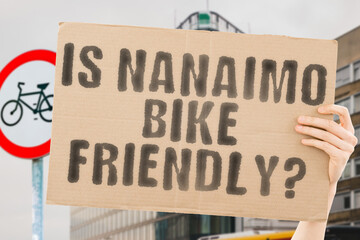 The question " Is Nanaimo bike friendly? " on a banner in men's hand with blurred background. Transportation. Zero waste. Bicycle lane. Streets. City. Safety. Insecure. Road signs. Dangerous