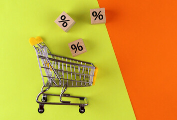 Empty shopping cart with wooden cubes with percent on orange and yellow background © Valeria F