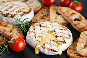 Grilled camembert, brie cheese with croutons, and cherry tomatoes on a dark background. - Powered by Adobe