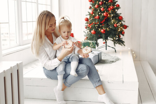 Mother with little daughter sitting near Christmas tree and and go donuts.
