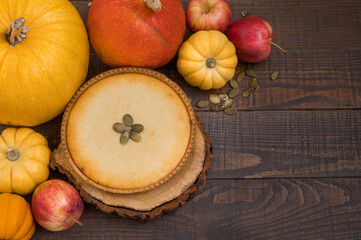 Pumpkin pie on wooden stands surrounded by pumpkins and apples on a dark wooden background.