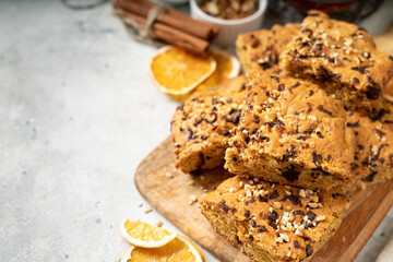 Pumpkin blondie bars with chocolate and walnuts close-up. Brownie pie slices on a serving wooden board on a light gray culinary background. Baking for Thanksgiving