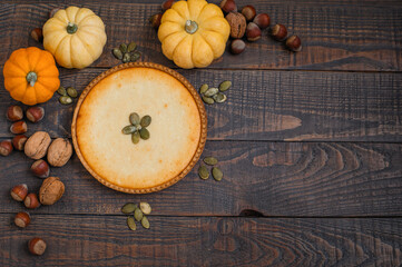 Pumpkin pie on wooden stands surrounded by pumpkins, walnuts and chestnuts on a dark background.
