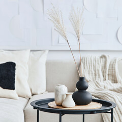 Stylish composition at fancy interior with wooden coffee table, dried flowers in vase, pillow, blanket, art painitngs and book in modern home decor. Details. Template.