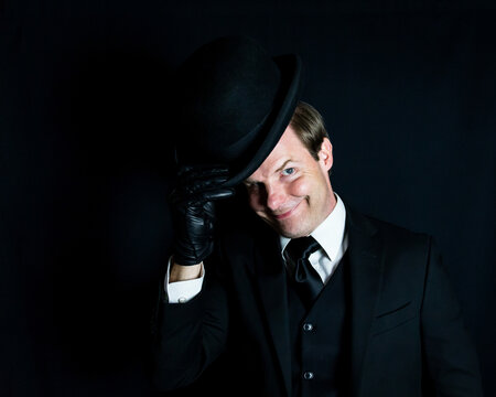 Portrait of Gentleman in Dark Suit Doffing Bowler Hat on Black Background. Retro Style and Vintage Fashion of Classic British Gentleman.