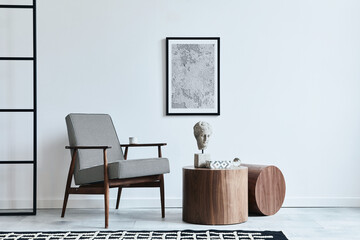 Stylish scandinavian composition of living room with design armchair, black mock up poster frame, carpet decor, wooden stool, decoration, loft wall and personal accessories in modern home decor