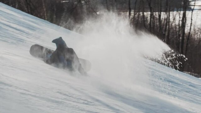 Snowboarder trying to perform a tripod trick and falls on the slope on sunny winter day at a ski resort. Snowboard buttering tricks.