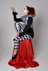 Full length  portrait of red haired  girl wearing a black and white clown jester costume,...
