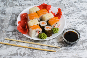 Sushi on a white plate on a light background with copy space. Delicious rolls with cheese, fish, sesame seeds, crab stick, wasabi, ginger and soy sauce.