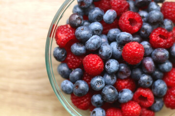 Glass bowl filled with raspberries and blueberries on wooden table. Top view.