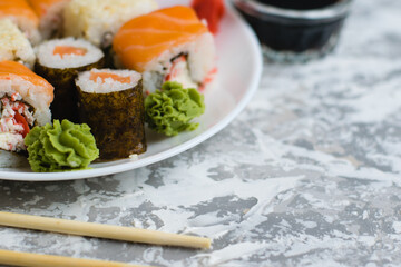 Sushi on a white plate on a light background with copy space. Delicious rolls with cheese, fish, sesame seeds, crab stick, wasabi, ginger and soy sauce.