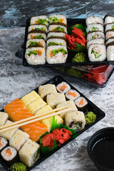 Several sets of sushi with wasabi and soy sauce in plastic packaging on a light gray background. Delicious rolls with shrimp, cucumber and spinach. Food delivery to your home or office.