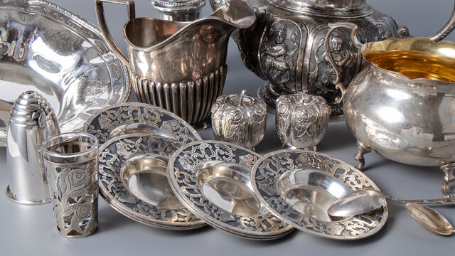 Lots of beautiful old silverware on a gray background. Sugar bowl, saucers, kettles and  salt shakers. 