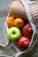 Crochet bag filled with butternut squash, pomegranates, apples and tangeriens. Top view.
