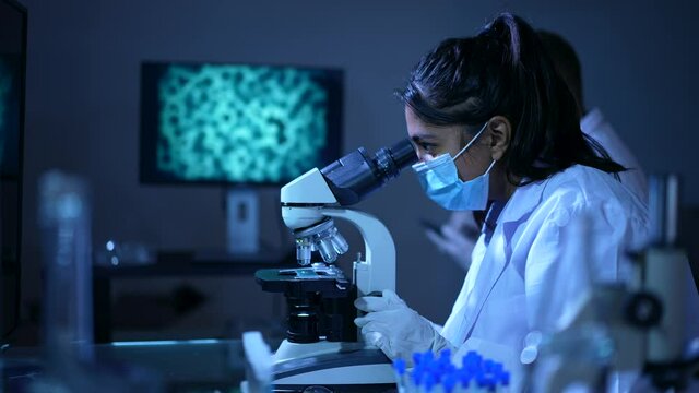 Asian Female Scientist Working In Laboratory Looking Through Microscope