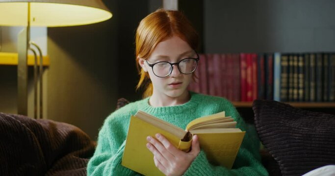 A girl in glasses reading a book with a dreamy look, sitting on the sofa