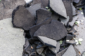 Pieces of asphalt concrete, close-up. Replacing the old pavement on a road or sidewalk. Dust, dirt, debris, and old leaves