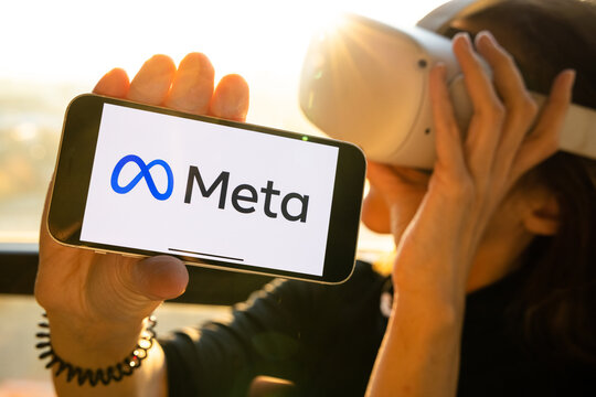 Meta Logo On The IPhone, Rebranding. Woman Holding Smartphone With New Facebook Logo Wearing Oculus VR Headset. 