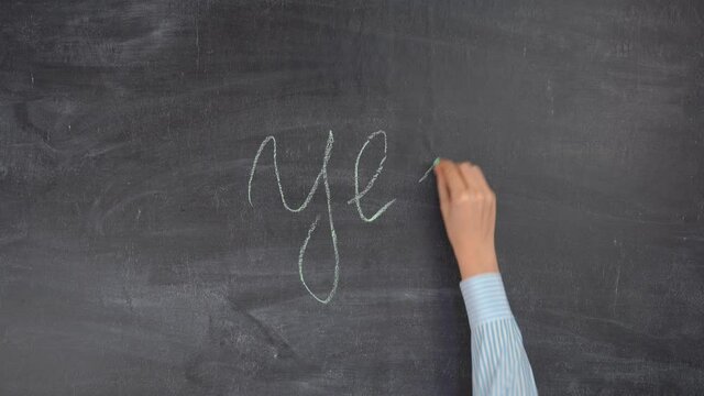 A woman's hand writes the word YES on a chalkboard with green chalk