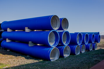 large diameter blue concrete pipes lie in the field.