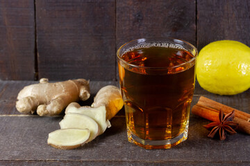 Glass of tea with ginger, lemon, cinnamon sticks and star anise on rustic wooden background.