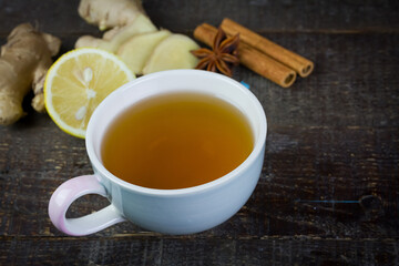 Cup of tea with ginger, lemon, cinnamon sticks and star anise on rustic wooden background.