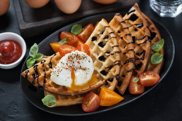 Waffles with poached egg and cherry tomatoes served on a black plate, selective focus, studio shot