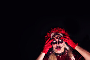 Closeup portrait of scary young woman dressed as a witch for Halloween, showing tongue, with her whites of eyes visible; isolated on black background