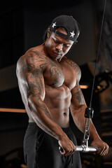 Strong and muscular dark skin man trains on modern equipment in gym. Portrait of muscular pumped up fitness trainer