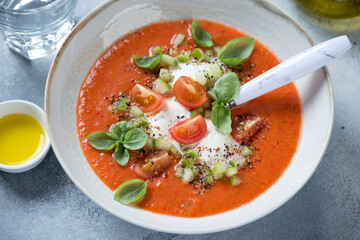 Plate of cold gazpacho made of red tomatoes and served with burrata cheese and green basil, studio shot, middle close-up