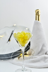 A festive glass with grapes on the background of a blurry clock and a bottle of champagne. Spanish...