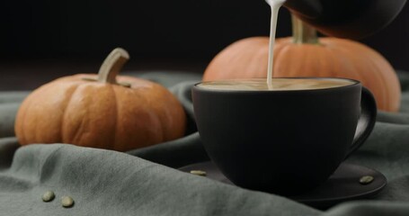 Slow motion making spiced pumpkin latte in black cup, pour steamed milk