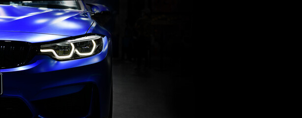 Fototapeta Front view of the LED headlights modern blue car on black background, obraz