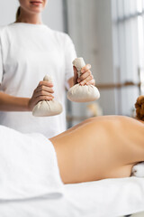 cropped view of masseur holding herbal bags while doing massage to client on massage table