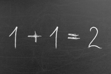 Math equation for pre-school students in the school handwritten on a blackboard. 1 plus 1 is 2. Educational and teaching concepts and backgrounds