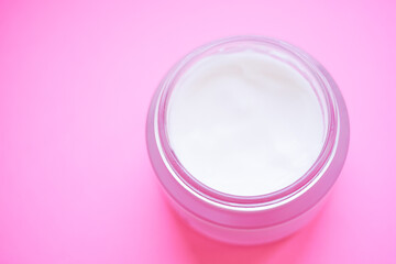 Open jar of cream on a pink table