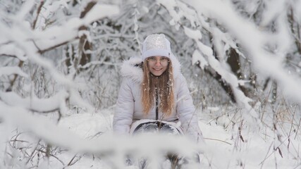 Portrait of a teenage girl sitting in a snowy fairy forest and throwing snow.