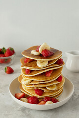 Traditional American stack of pancakes with bananas, strawberries and syrup on a table for breakfast or lunch 