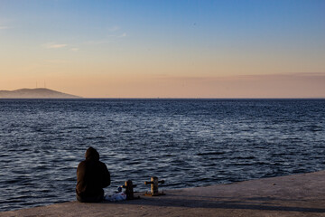 Naklejka na ściany i meble Person sitting and looking at the sunset in burgazada Istanbul, turkey