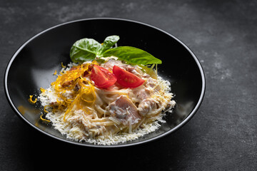 Pasta with meat cheese and basil on a black plate