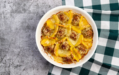 Potato with meatballs in a white baking dish on a dark grey background. Top view, flat lay
