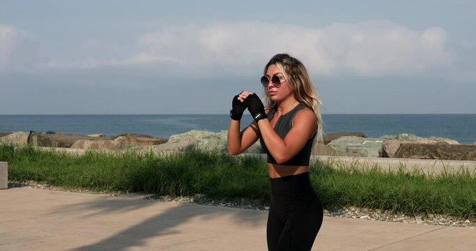 Athletic young woman shadow boxing by the sea. Tae bo training.