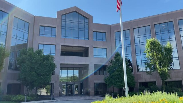 Generic Day Time DX Exterior establishing shot of generic office building with American Flag breeze in the United States.  Sunny day with blue sky and sun reflection in windows of structure.